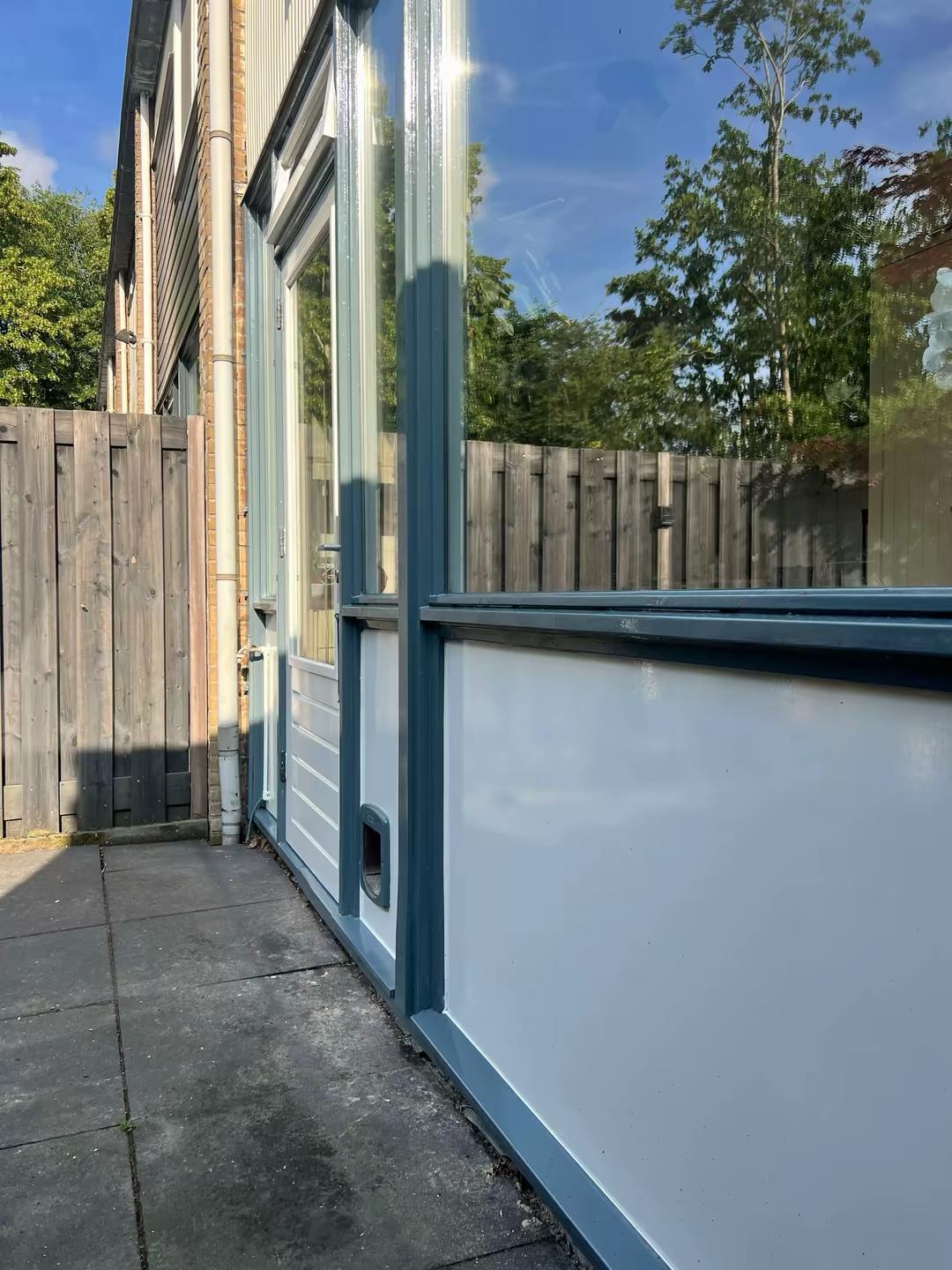 Zijkant van achterdeur en raam met blauw geschilderde kozijnen
