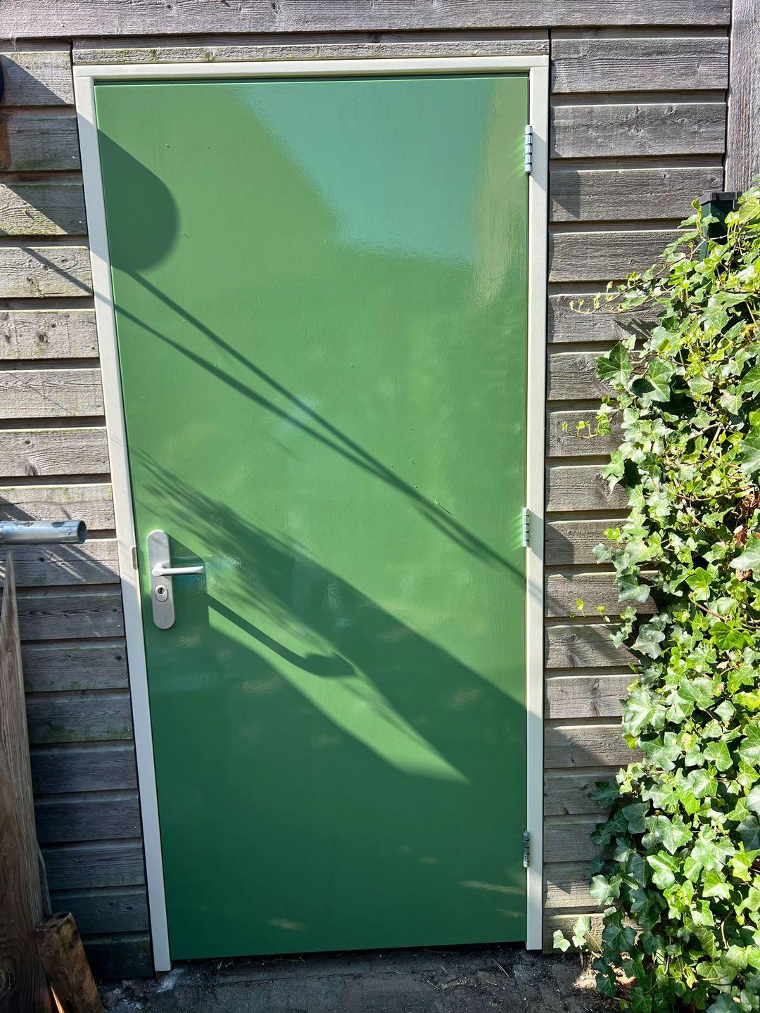 Groen geschilderde schuurdeur met wit kozijn