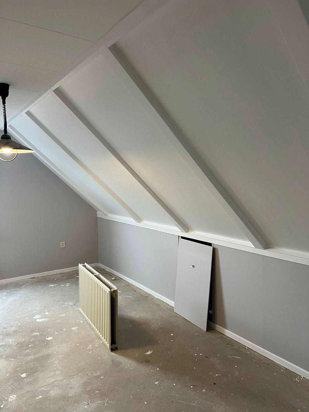 Zolderkamer met schuine dakconstructie en strak afgewerkte grijze muren