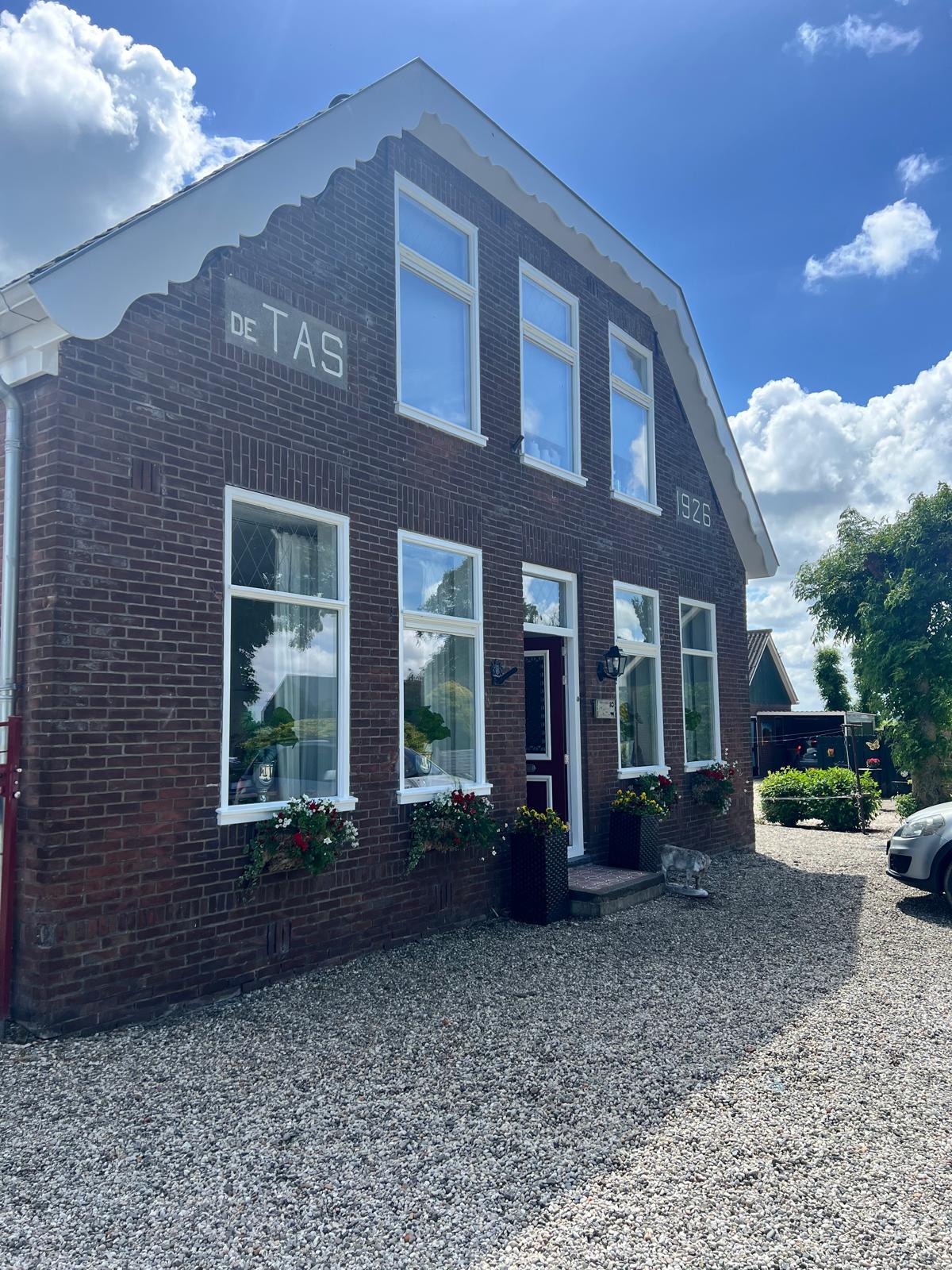 Voorgevel van de karakteristieke boerderij met witte kozijnen en bloembakken