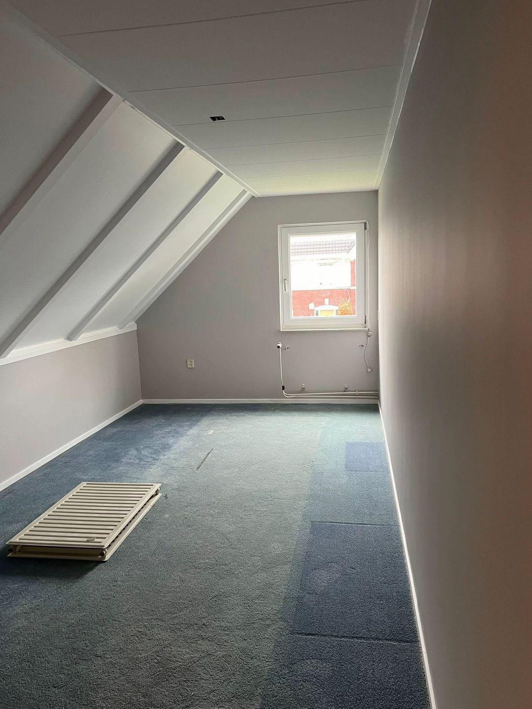 Zolderkamer met schuine dakconstructie, blauw tapijt en radiator